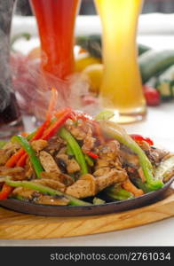 original fajita sizzling smoking hot served on iron plate ,with selection of beer and fresh vegetables on background ,MORE DELICIOUS FOOD ON PORTFOLIO