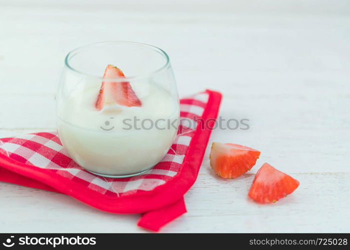 Original flavor yogurt with fresh strawberry in clear glass on white wood background