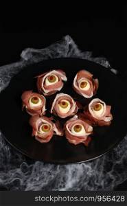 Original Halloween snacks. Eyeballs cooked from jamon with mozzarella, olives stuffed with red pepper