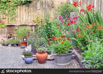 Ornamental garden with colorful plants in flowerbed and wooden table with chairs. Ornamental garden with colorful plants in flowerbed and wooden table