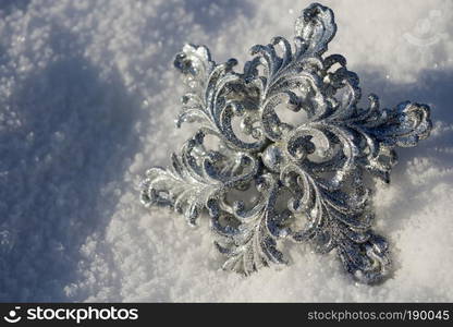 Ornamental silver snowflake glittering on fresh white snow.