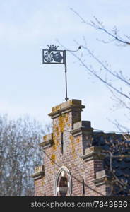 Ornamental weather vane with crown and shields on historical brick wall