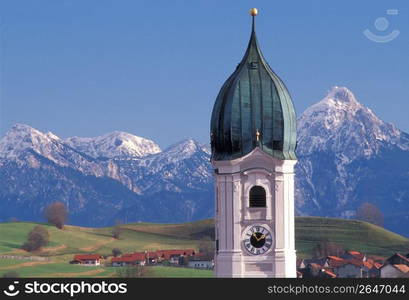 Ornate dome of clock tower over quaint remote village with snow-covered mountains in background