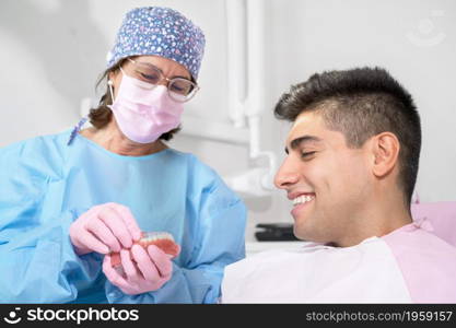 Orthodontist holding invisible retainer for teeth alignment. In clinic shows patient removable transparent plastic aligners or invisalign use and benefit. High quality photo.. Orthodontist holding invisible retainer for teeth alignment. In clinic shows patient modern dental technology - removable transparent plastic aligners or invisalign use and benefit.