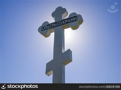 Orthodox cross against the blue sky and the sun. Cross in the backlight of the sun. Symbol of the Christian faith. The inscription on the cross  salvation and preservation. Krasnodar, Russia - April 29, 2017  Orthodox cross against the blue sky and the sun. Cross in the backlight of the sun. Symbol of the Christian faith. The inscription on the cross  salvation and preservation
