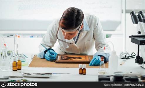 Orthodox Icon Restoration and conservation. Female conservation uses brush to retouch damages on a painting surface.. Orthodox Icon Restoration and conservation