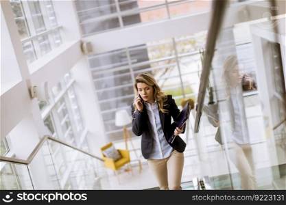 ortrait of young businesswoman climbs upstairs in a business building and uses a cell phone