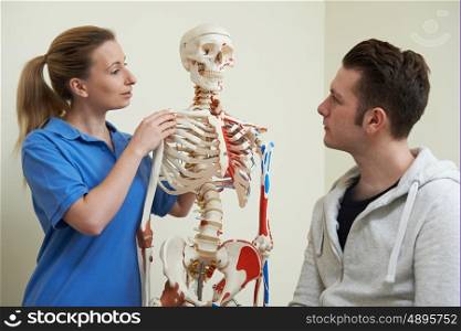 Osteopath Discussing Injury With Patient Using Skeleton