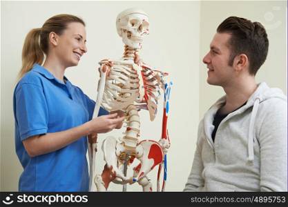 Osteopath Discussing Injury With Patient Using Skeleton