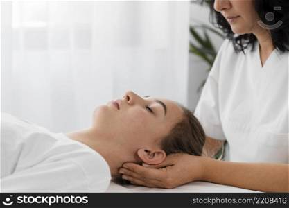 osteopathist treating female patient by massaging her face