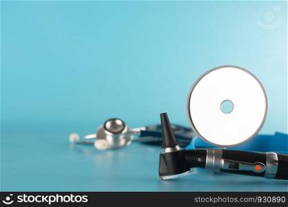 Otoscope with stethoscope and reflector mirror on blue background.