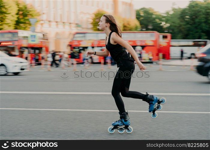 Outdoor activities for being healthy and fit. European woman in good physical shape rides on rollers rolleblades on inline skates dressed in active wear has active rest. Sporty lifestyle concept