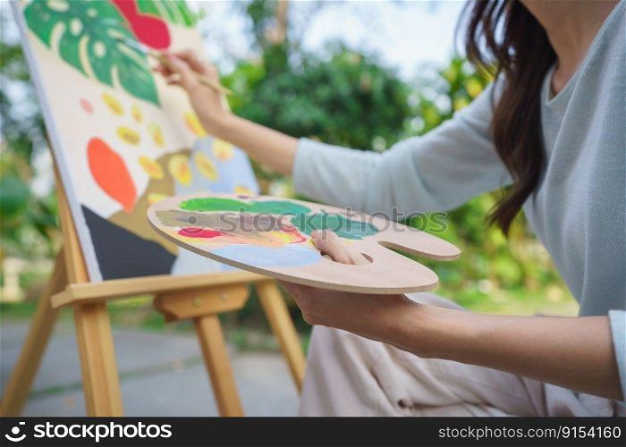 Outdoor activity concept, Female artist painting on canvas with paintbrush and watercolor in garden.