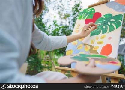 Outdoor activity concept, Female artist painting on canvas with paintbrush and watercolor in garden.