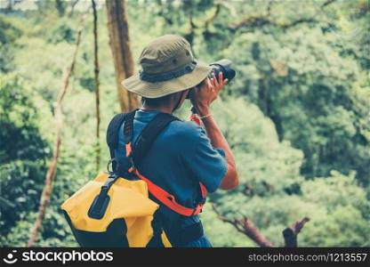 Outdoor adventure and Traveler man holding camera on nature forest tourist on holiday vacation trips adventurous backpacking travel hike / Man photographer taking photo Modern outdoor excursions