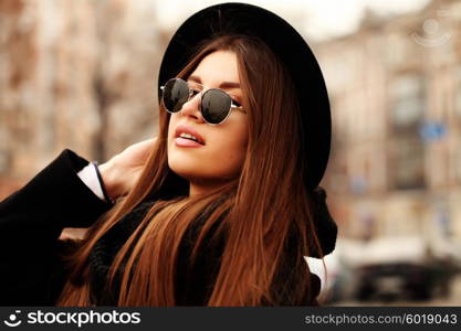 Outdoor fashion image of stylish beautiful brunette young woman wearing scarf, sunglasses and vintage hat, walking on the street