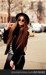 Outdoor fashion image of stylish beautiful brunette young woman wearing scarf, sunglasses and vintage hat, walking on the street