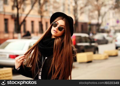 Outdoor fashion image of stylish beautiful brunette young woman wearing scarf, sunglasses and vintage hat, walking on the street