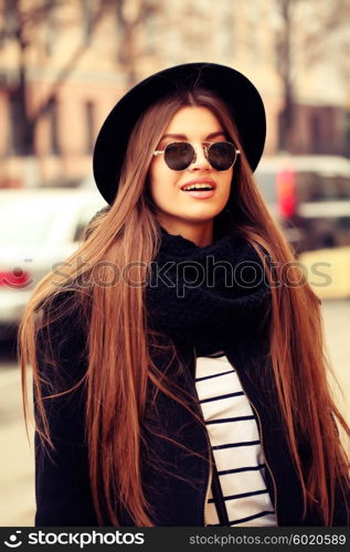 Outdoor fashion image of stylish beautiful brunette young woman wearing scarf, sunglasses and vintage hat, walking on the street