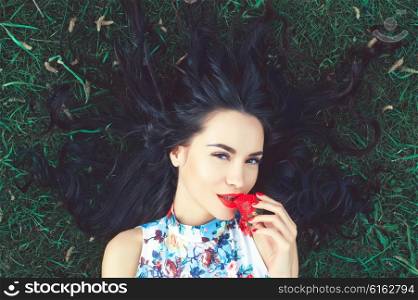 Outdoor fashion photo of beautiful young lady on grass with strawberry in mouth