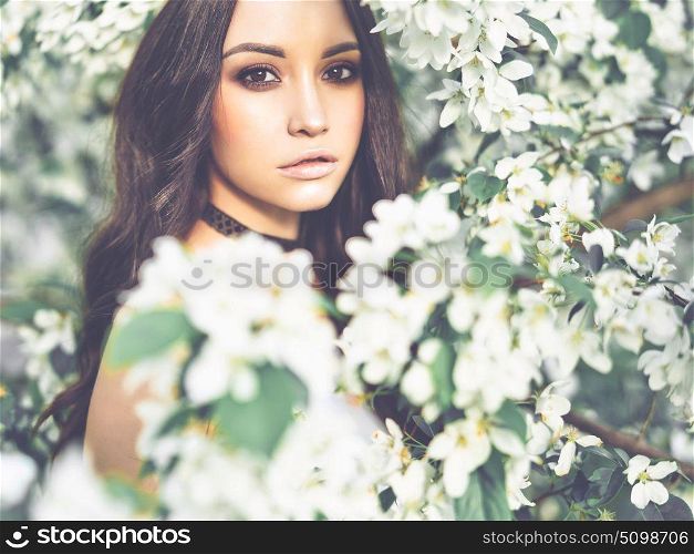 Outdoor fashion photo of beautiful young woman surrounded by flowers of apple-tree. Spring blossom. Summer vibes