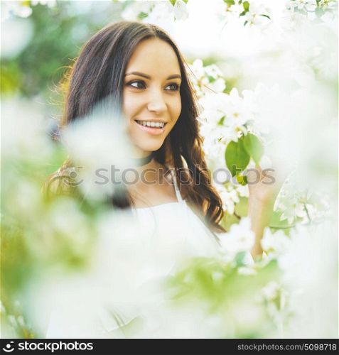 Outdoor fashion photo of beautiful young woman surrounded by flowers of apple-tree. Spring blossom