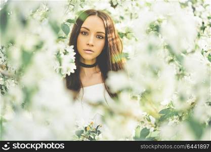 Outdoor fashion photo of beautiful young woman surrounded by flowers of apple-tree. Spring blossom. Summer vibes