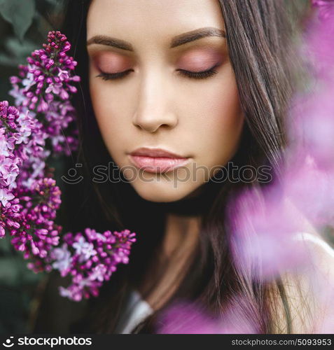 Outdoor fashion photo of beautiful young woman surrounded by flowers of lilac. Spring blossom