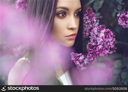 Outdoor fashion photo of beautiful young woman surrounded by flowers of lilac. Spring blossom