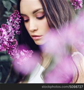 Outdoor fashion photo of beautiful young woman surrounded by flowers of lilac. Spring blossom