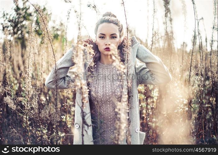 Outdoor fashion photo of young beautiful lady in autumn landscape with dry flowers
