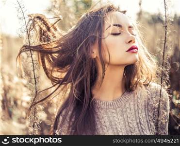 Outdoor fashion photo of young beautiful lady in autumn landscape with dry flowers. Knitted sweater, wine lipstick. Warm Autumn. Warm Spring