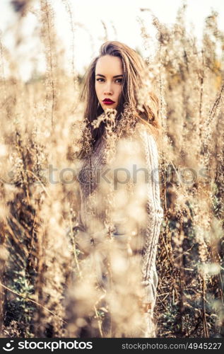 Outdoor fashion photo of young beautiful lady in autumn landscape with dry flowers. Knitted sweater, wine lipstick. Warm Autumn. Warm Spring