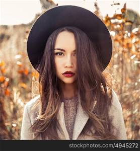 Outdoor fashion photo of young beautiful lady in autumn landscape with dry flowers. Gray coat, black hat, wine lipstick. Warm Autumn. Warm Spring