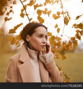 Outdoor fashion photo of young beautiful lady in beige coat in autumn landscape