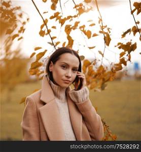 Outdoor fashion photo of young beautiful lady in beige coat surrounded autumn leaves