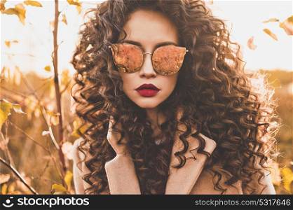 Outdoor fashion photo of young beautiful lady in sunglasses surrounded autumn leaves. Fashion lookbook. Warm autumn. Fall vibes. Warm winter