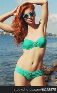 Outdoor fashion portrait of beautiful red-haired sexy woman with perfect athletic body enjoy your holiday. Wearing bright stylish bikini and sunglasses. Photo toned style instagram filters