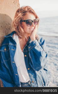 Outdoor fashion portrait of stylish girl wearing trendy sunglasses and jeans jacket on the beach.. Outdoor fashion portrait of stylish woman on the beach.