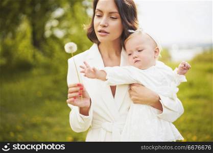 Outdoor fashion portrait of young beautiful mother and little cute daughter blowing to dandelion on green meadow. Spring image