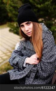 Outdoor fashion portrait of young pretty funny girl wearing trendy fall outfit, black hat, grey coat and leather bag. Cold season. Warm clothes. Young happy woman having fun outdoor