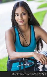 Outdoor fitness portrait of a beautiful Indian Asian young woman or girl outside in summer sunshine riding cycling her bicycle