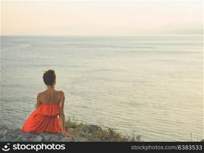 Outdoor lifestyle photo of woman in red dress looking at sea. Travel background. Tourism.