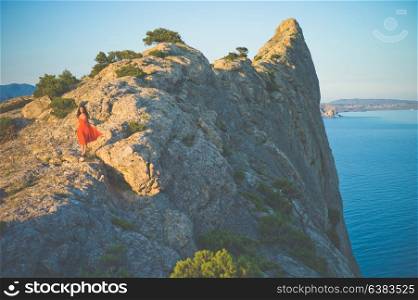 Outdoor lifestyle photo of woman in red dress walking on rock. Travel background. Tourism.