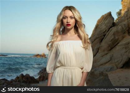 Outdoor lifestyle portrait of beautiful young blonde woman on the beach. Natural beauty. Travel and youth. Lady in white dress