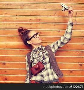 Outdoor lifestyle portrait of pretty funny hipster woman making photo. Retro photographer. Modern urban girl has fun with vintage photo camera, wooden background.
