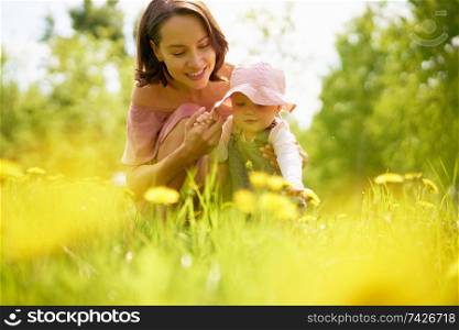 Outdoor lifestyle portrait of young beautiful mother and little cute daughter on a meadow with dandelions. Summer image