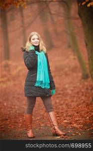 Outdoor nature leisure foliage vegetation concept. Smiling lady walking through park. Young blonde taking a walk in autumnal woodland wearing blue scarf.. Smiling lady walking through park.