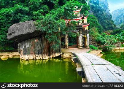 Outdoor park landscape with lake and stone bridge. Gate entrance to ancient Bich Dong pagoda complex. Ninh Binh, Vietnam travel destination