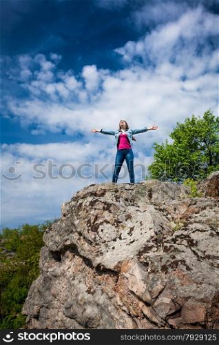 Outdoor photo of beautiful woman standing on top of high cliff with stretched out hands